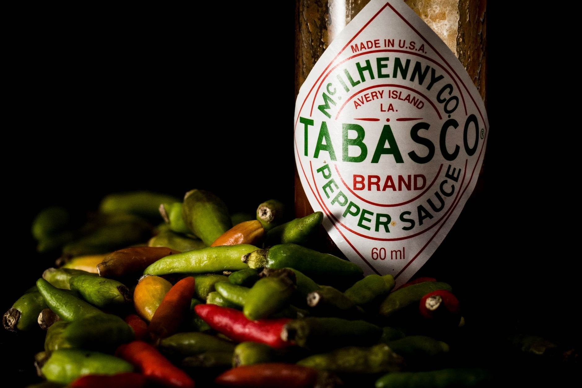 Craft hot sauce bottle surrounded by fresh chili peppers on a dark surface